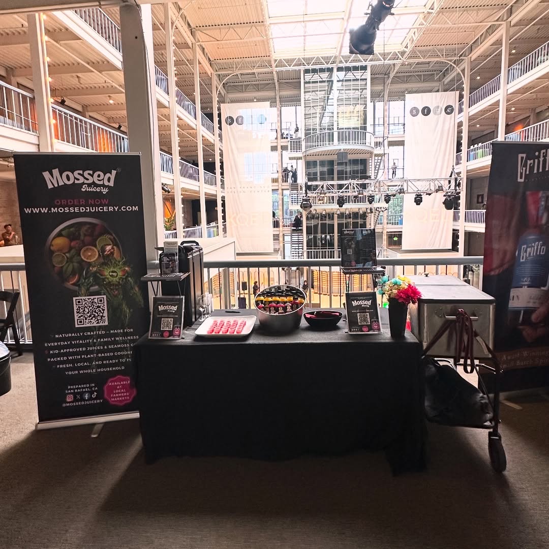 Mossed Juicery market booth with branded banner, juice samples, and chilled bottles at the San Francisco Design Center